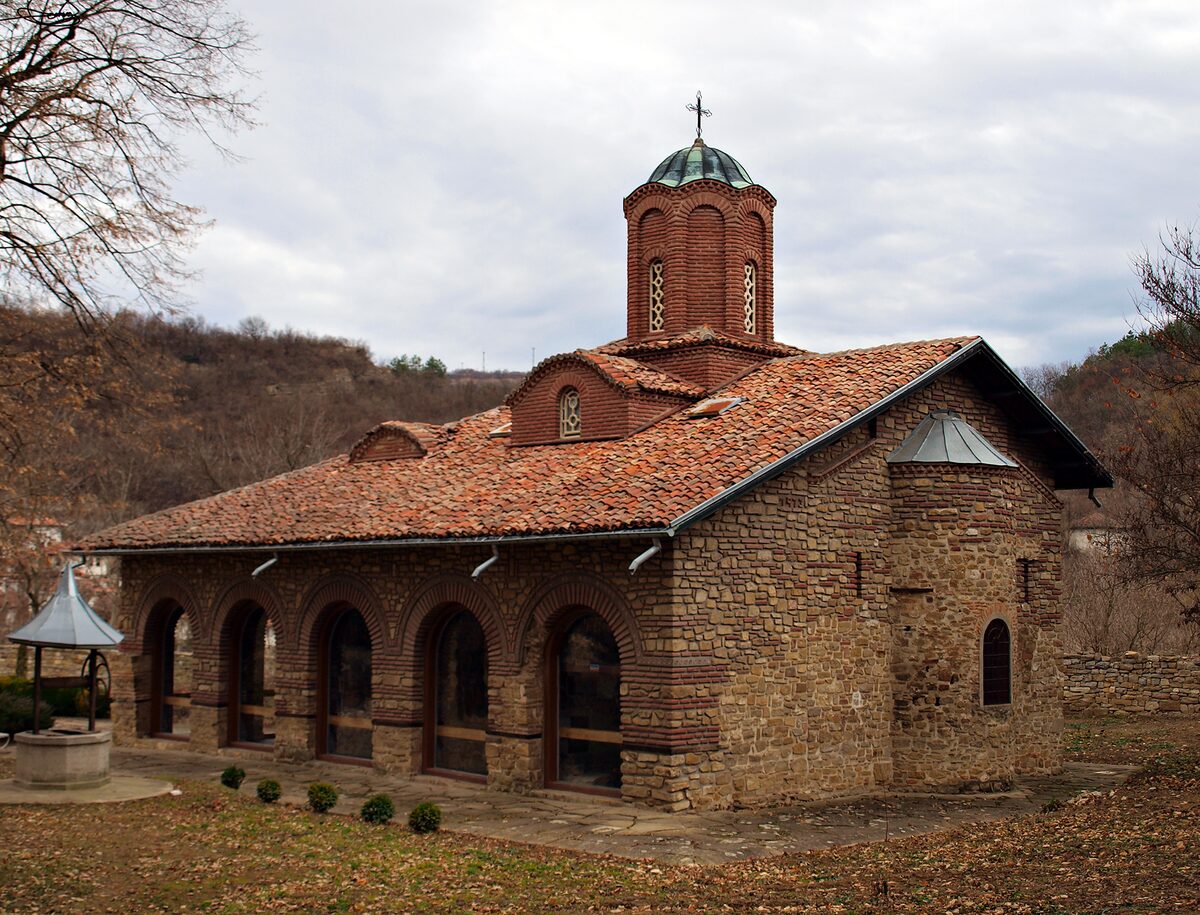 The small medieval Church of Sts Peter and Paul, built of banded stone and brick with a tiled roof and a brick drum dome, under an autumn sky.