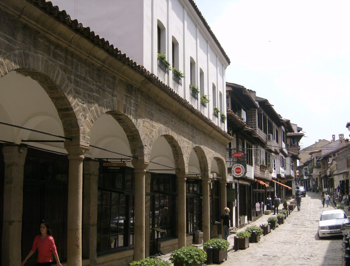 The arcaded stone front of the Hadji Nikoli Inn along a cobbled lane of the Samovodska charshia, lined with Revival-era craft shops.