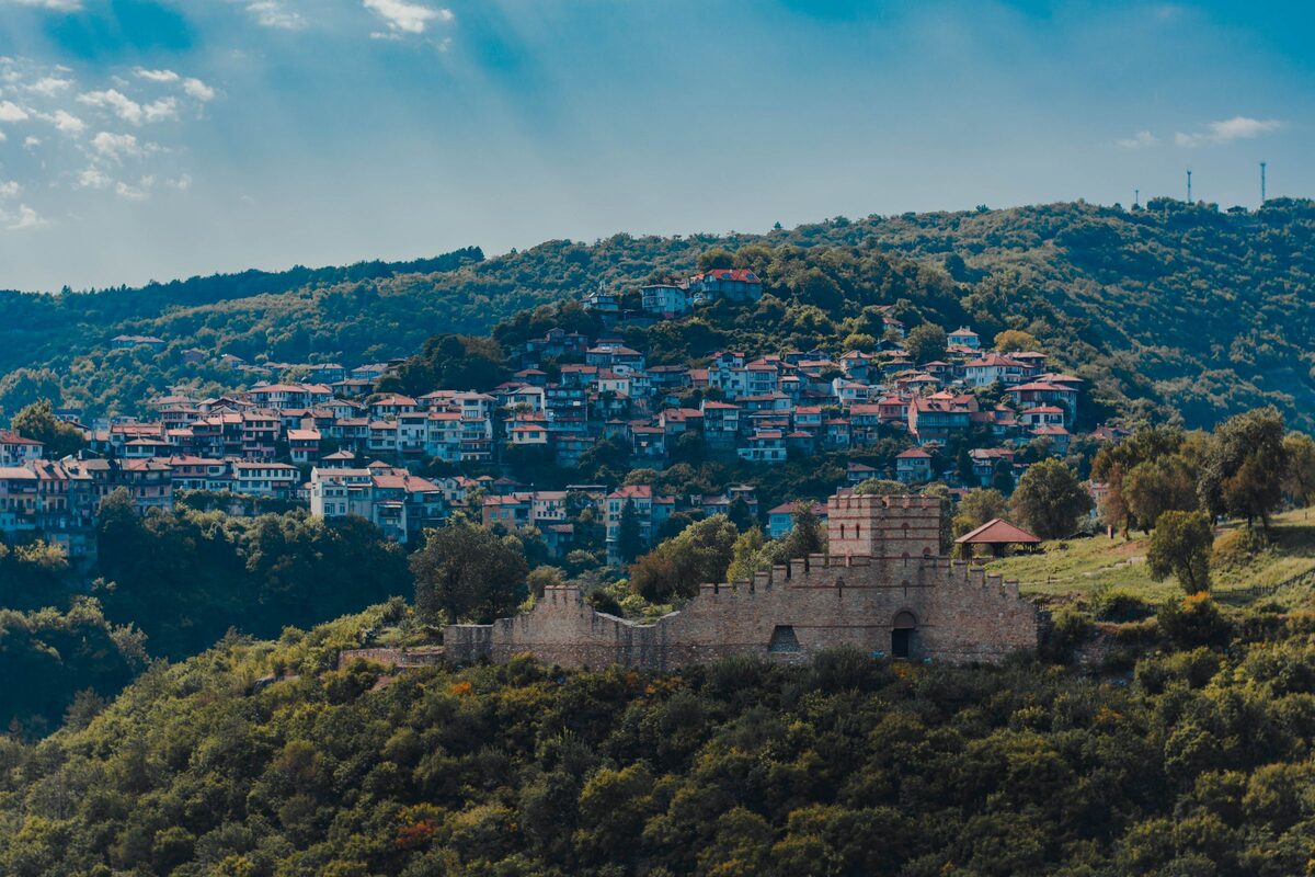 The restored stone walls and gate tower of Trapezitsa fortress on its wooded hill, with Veliko Tarnovo's houses climbing the slope behind.
