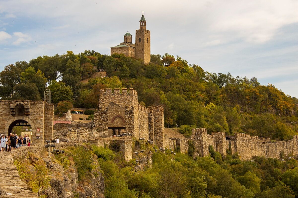 The stone gate towers and walls of Tsarevets fortress, with the Patriarchal Church crowning the wooded hill above.
