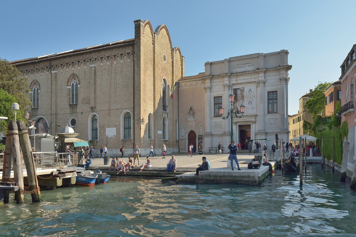 The facade of the Gallerie dell'Accademia and the church of the Carità on the Grand Canal, with people sitting on the landing stage