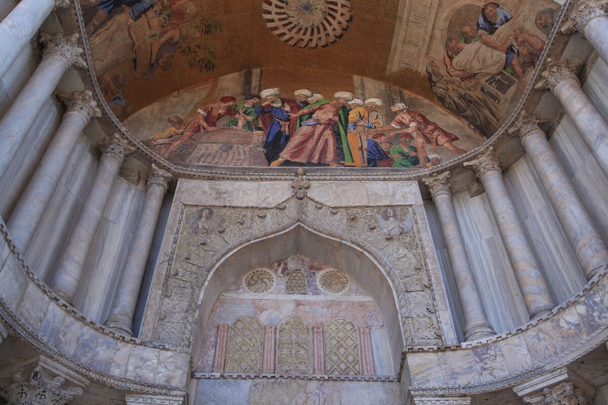 A golden mosaic in a carved marble arch over one of the doorways of St Mark's Basilica, with columns on both sides