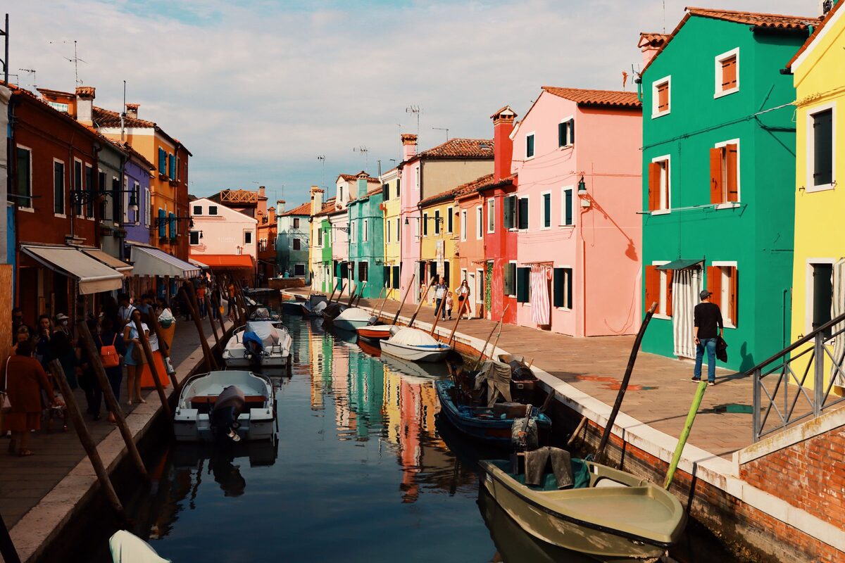 A canal in Burano lined with brightly painted houses in red, blue, yellow and green, with small boats moored along the side