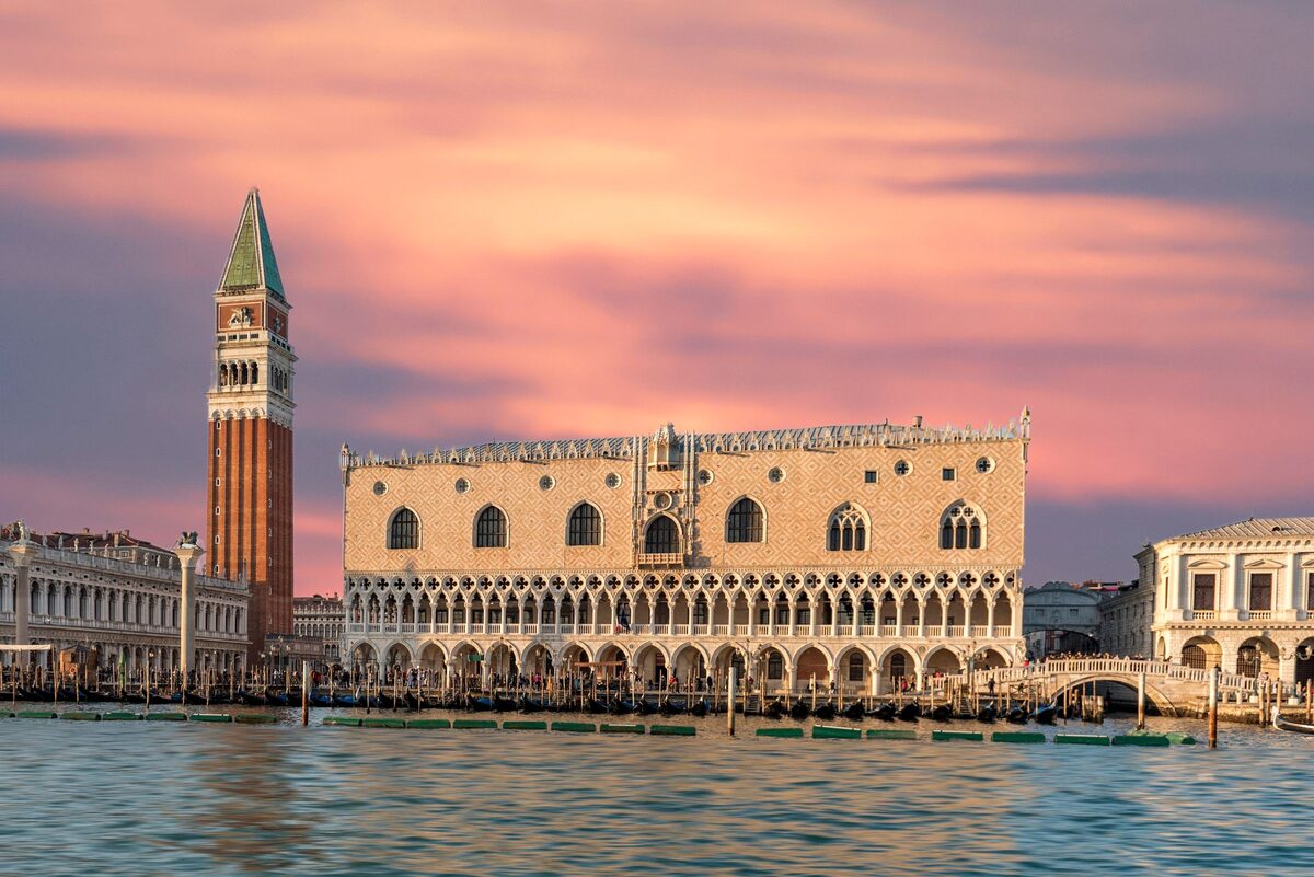 The Doge's Palace and the brick Campanile of St Mark's seen from the water at sunset, under a pink and orange sky