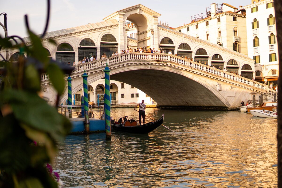 The white stone arch of the Rialto Bridge over the Grand Canal in warm evening light, with a gondola passing beneath