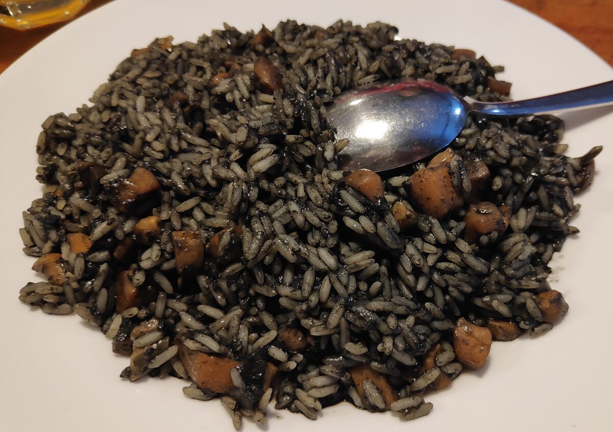 A plate of black risotto made with cuttlefish ink, with pieces of cuttlefish and a spoon