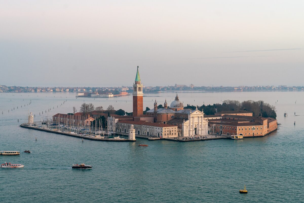 Aerial view of the island of San Giorgio Maggiore with its white church, bell tower and small marina, surrounded by the lagoon