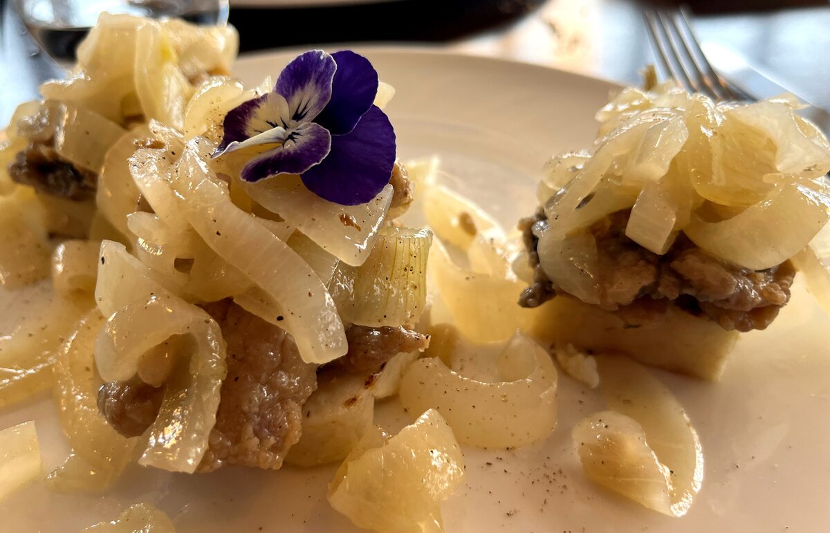 Fried sardine fillets under a heap of soft, sweet-and-sour white onions, topped with a purple pansy