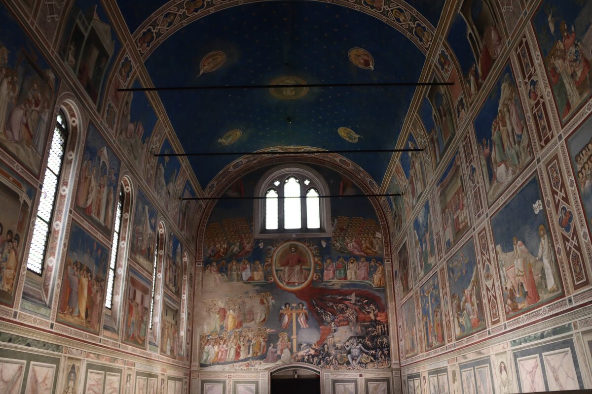 Inside the Scrovegni Chapel in Padua, its walls covered in Giotto's frescoes in rows of panels under a deep blue starry ceiling
