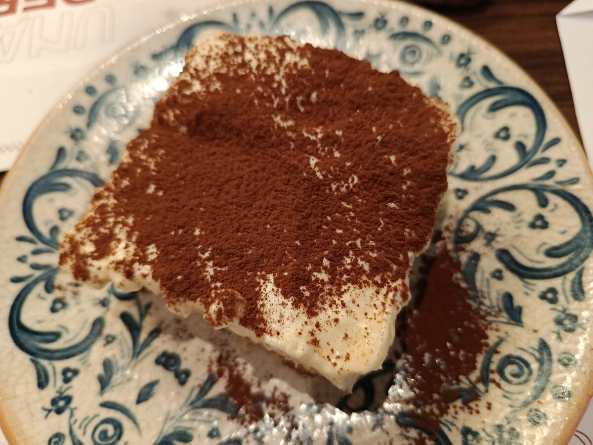 A slice of tiramisu dusted with cocoa on a blue and white patterned plate
