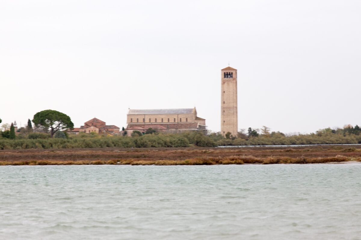 The cathedral of Santa Maria Assunta and its tall brick bell tower on Torcello, seen across the marshes and water of the lagoon
