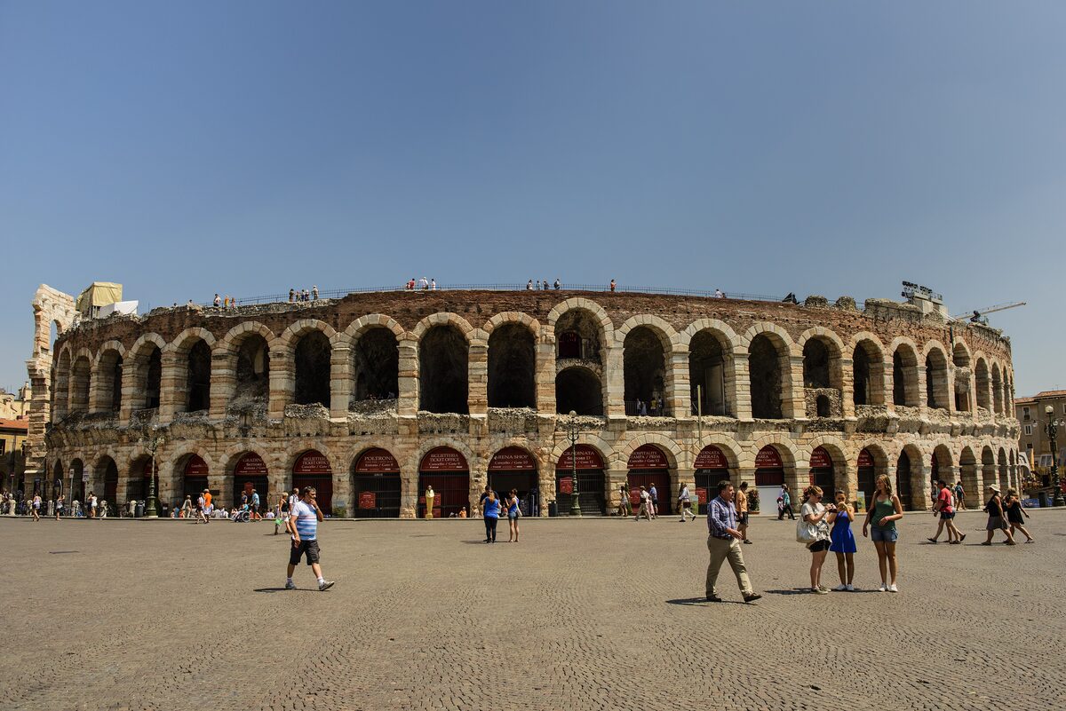 The Roman Arena of Verona with its rows of stone arches, across the wide paving of Piazza Bra