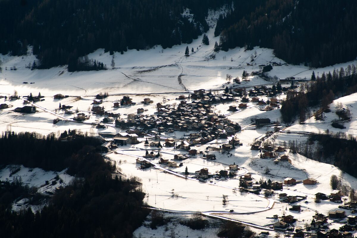 The village of Bruson under deep snow, with dark pine forest around it