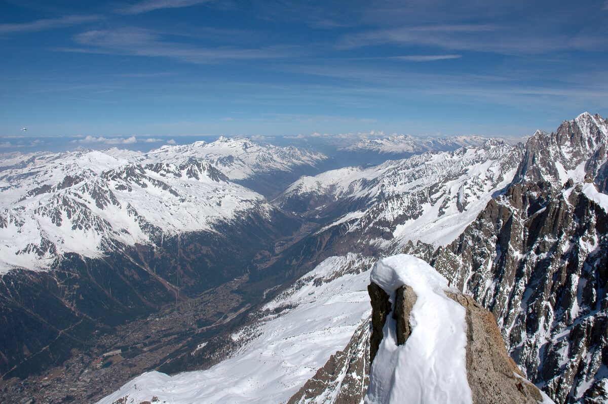 The Chamonix valley seen from the Aiguille du Midi, with snow-covered ridges and a snowy rock ledge in the foreground