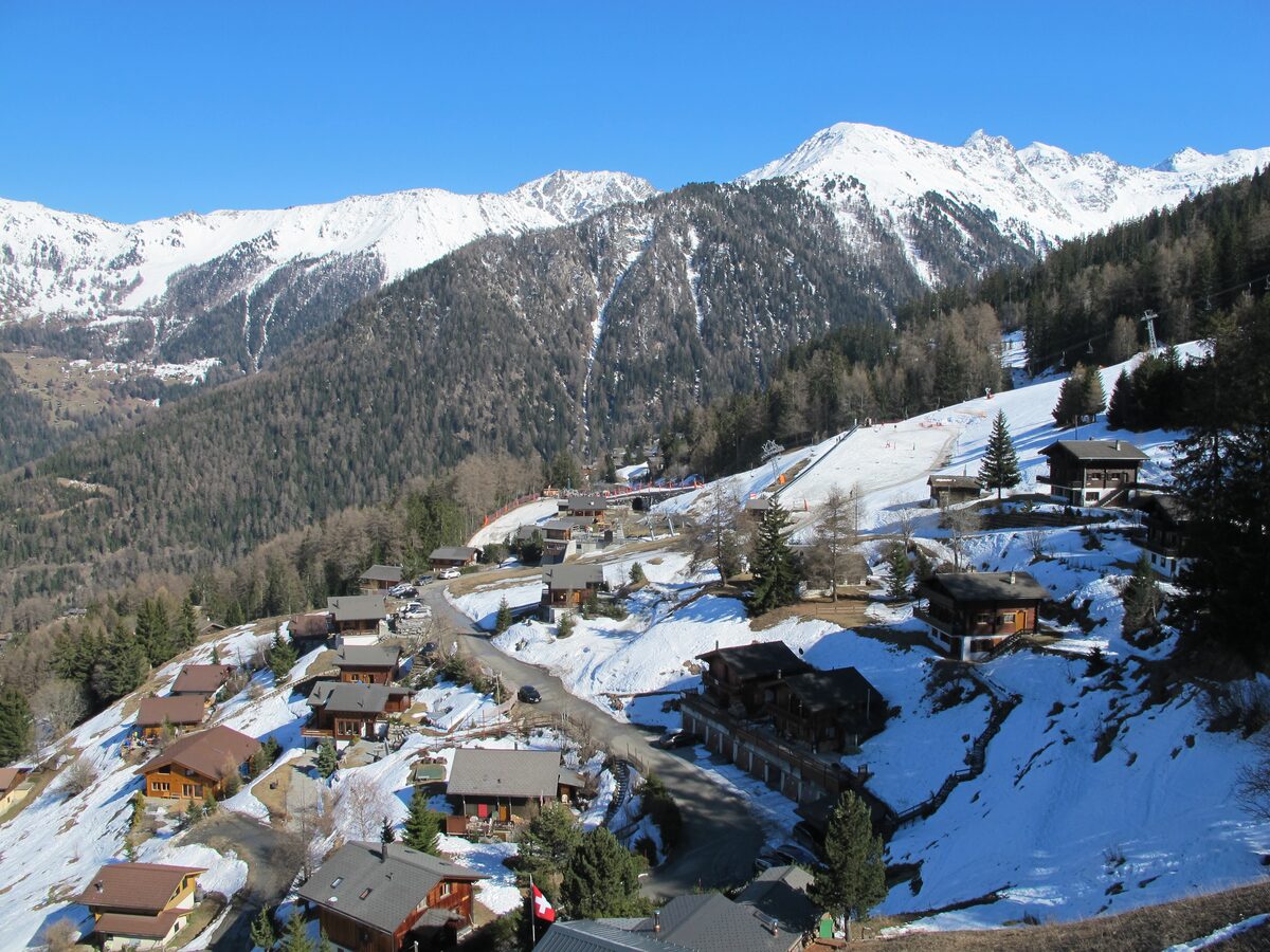 Wooden chalets of La Tzoumaz on a snowy hillside, with forested slopes and snow-capped peaks behind