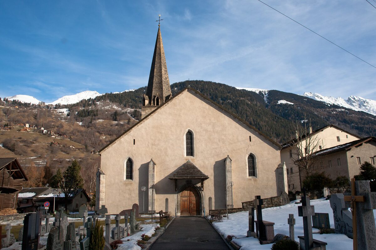 The church of Le Châble with its spire, a graveyard in the foreground and snow on the hills behind