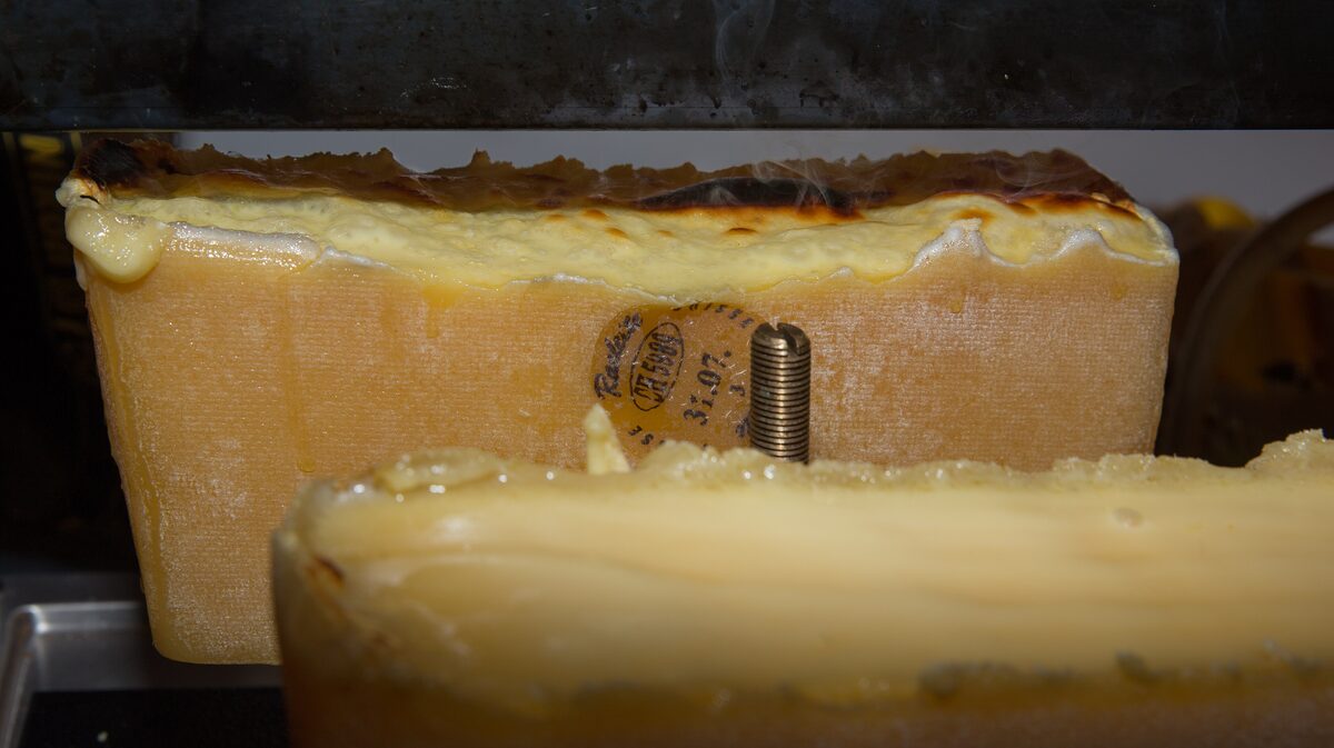 Two halves of a raclette cheese wheel melting under the heater