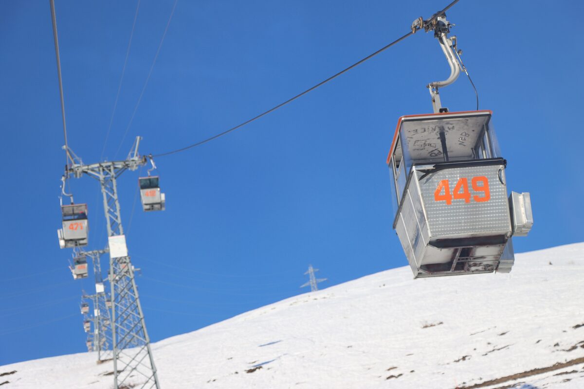 Old gondola cabins, one numbered 449, on a cable above a snowy slope under a deep blue sky