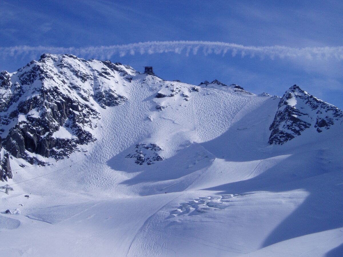 A steep snowy slope covered in moguls under rocky peaks