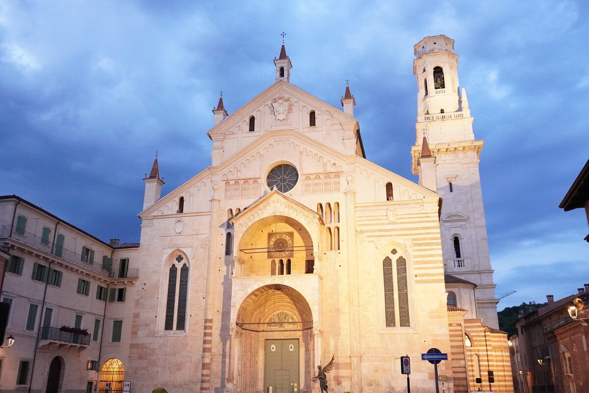 Verona Cathedral's pale striped facade and bell tower lit at dusk