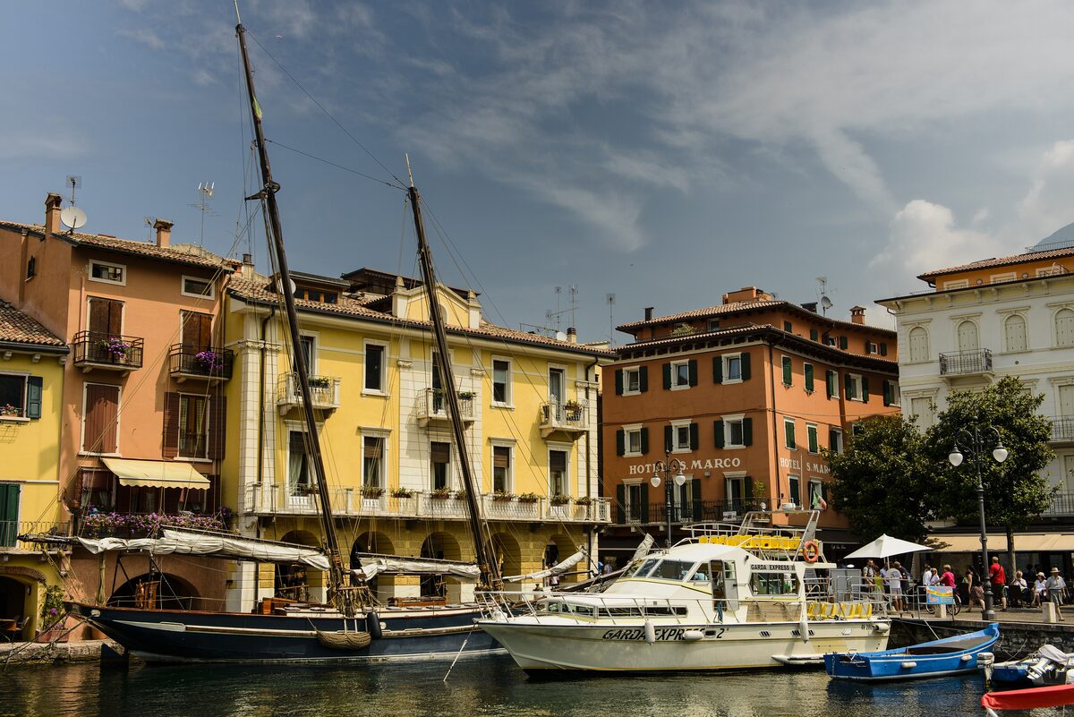 Boats and tall-masted sailing barges in Malcesine harbor below the mountains