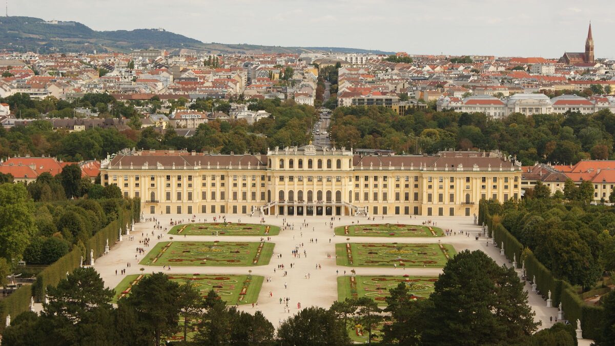 Aerial view of Schönbrunn Palace, its long yellow facade and the formal gardens in front, with the city behind