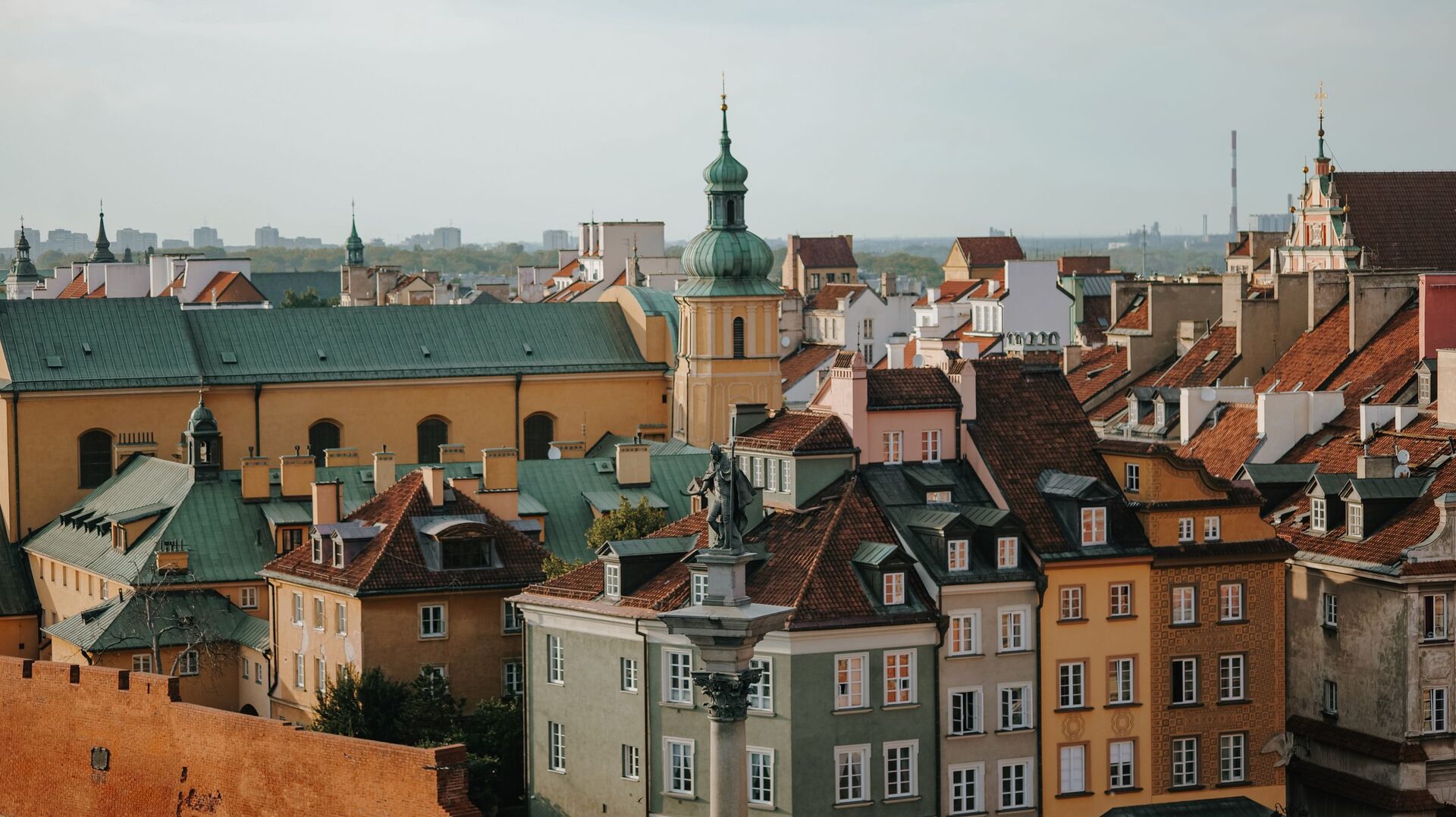 The rooftops of Warsaw's Old Town with green copper domes and church towers, and Sigismund's Column on Castle Square