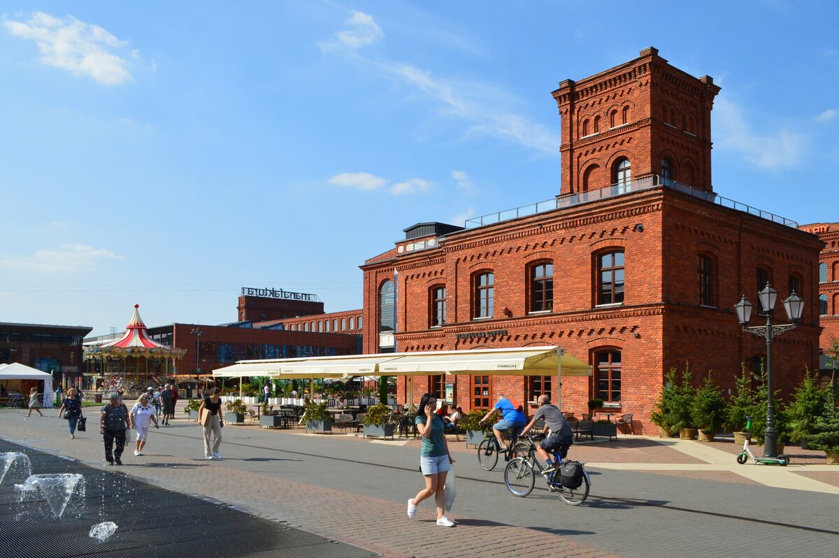 A red brick factory building at Manufaktura in Łódź, with people walking and cycling in front
