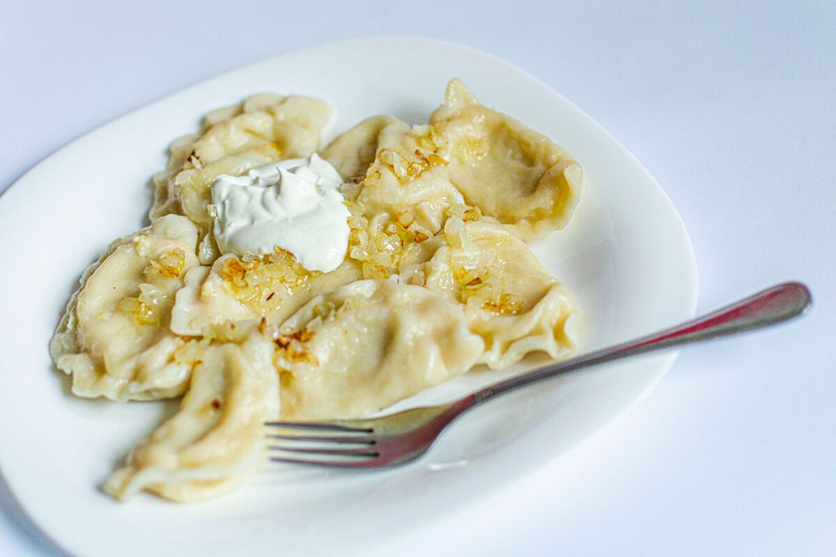 A plate of pierogi topped with fried onions and a spoonful of sour cream