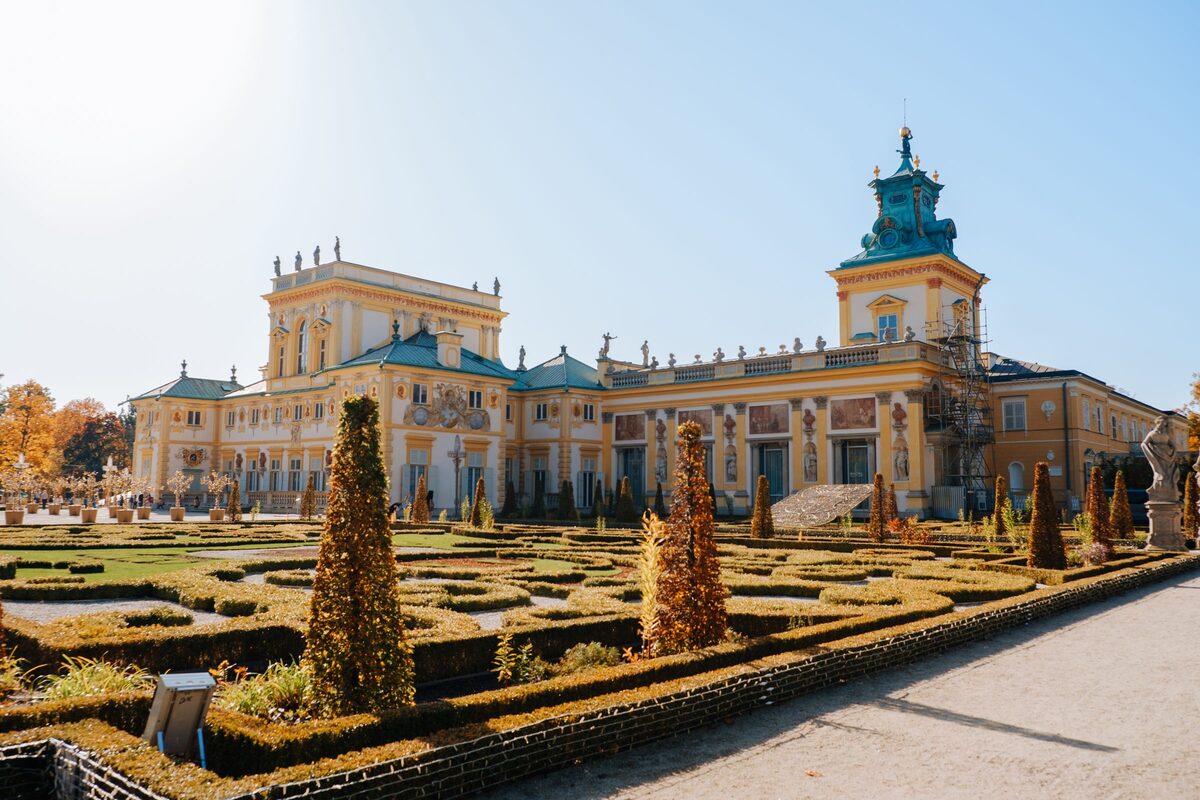 Wilanów Palace with its yellow baroque facade, statues and green tower domes, behind clipped box hedges in the garden
