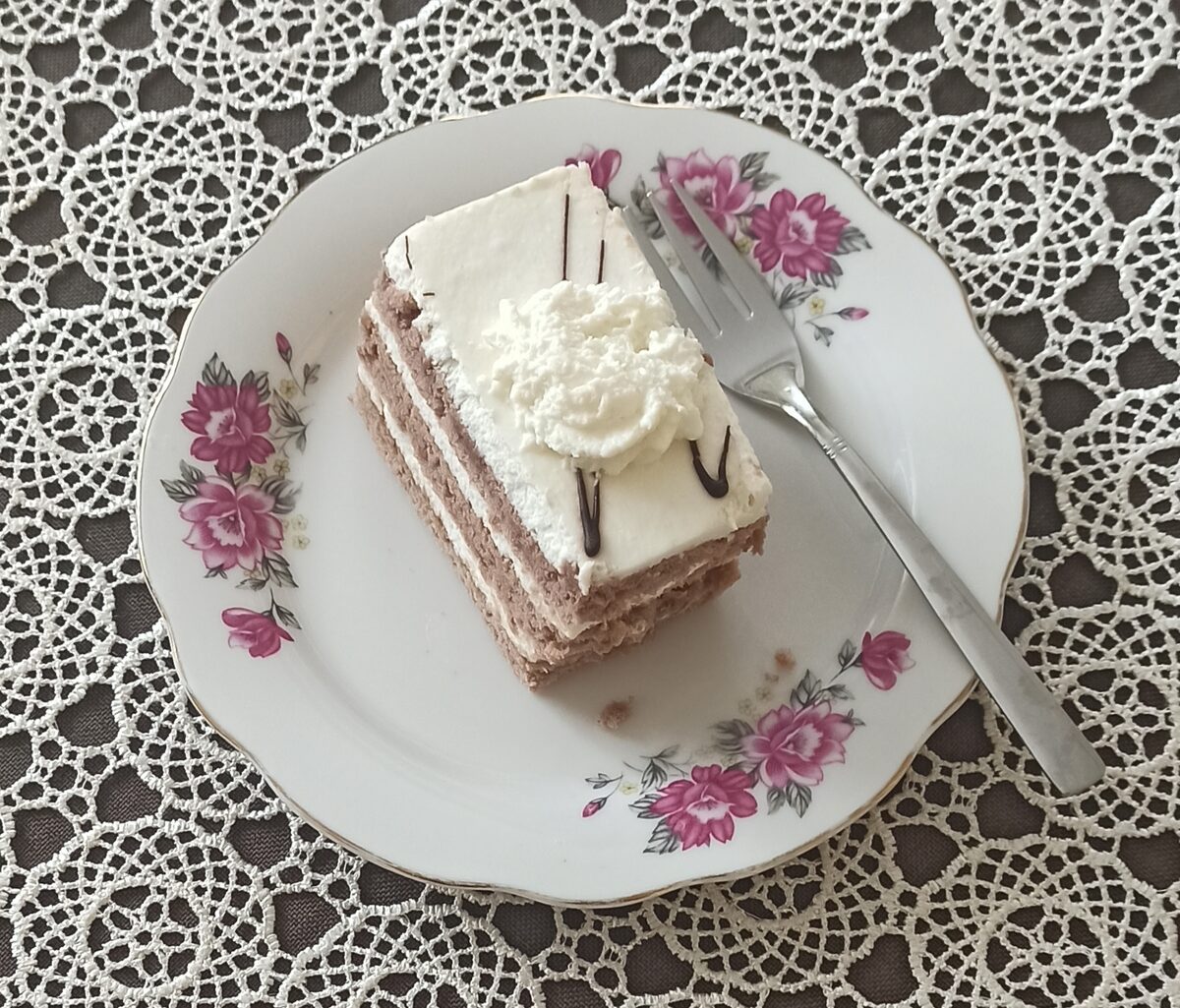A slice of wuzetka, chocolate sponge cake layered with whipped cream, on a flowered plate