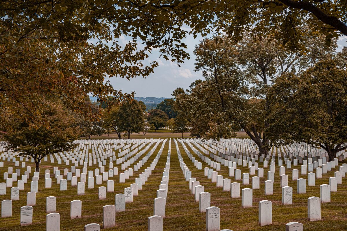 Rows of white headstones under autumn trees at Arlington National Cemetery
