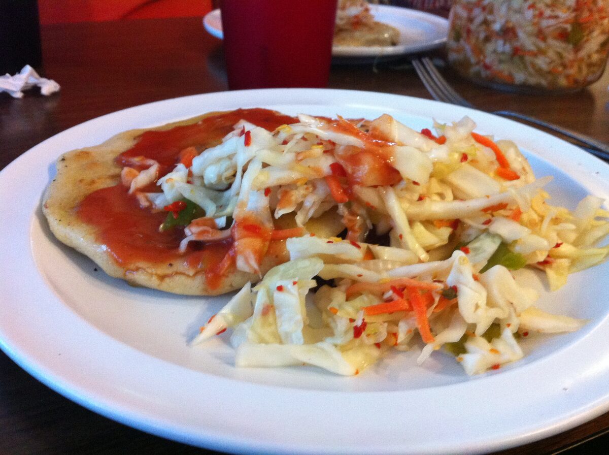 A pupusa topped with curtido cabbage relish and red salsa