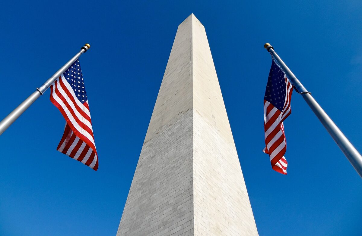 Washington Monument obelisk between two American flags against a deep blue sky