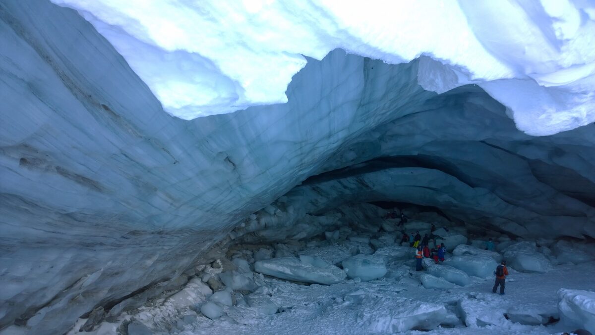Visitors standing in a large blue ice cave under the Blackcomb Glacier