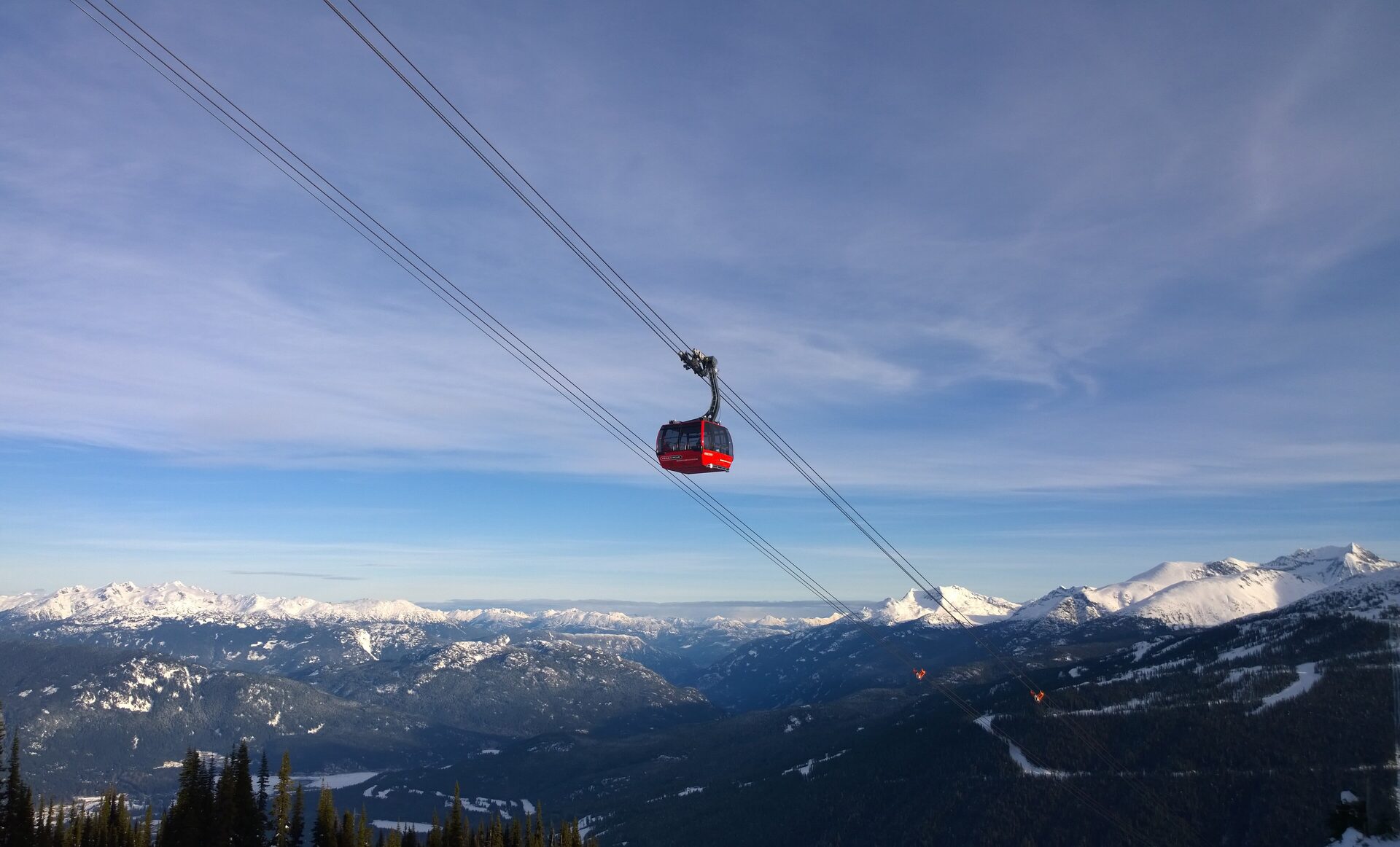 A red Peak 2 Peak gondola cabin on its cables above the snowy Coast Mountains on a clear winter day