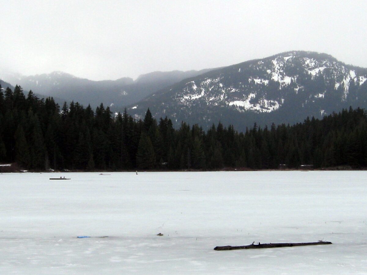 Lost Lake frozen and covered in snow, with a snow-dusted forested mountain behind