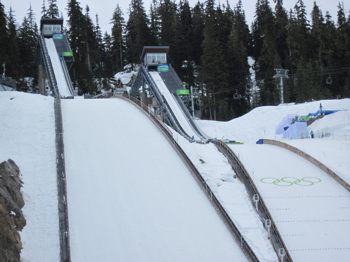 The Olympic ski jumps at Whistler Olympic Park with snow on the landing slopes and the Olympic rings painted on the ground