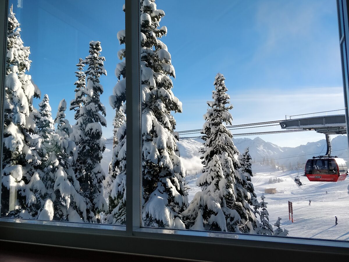A red Peak 2 Peak gondola cabin at its station seen through a window onto snow-covered trees and ski runs