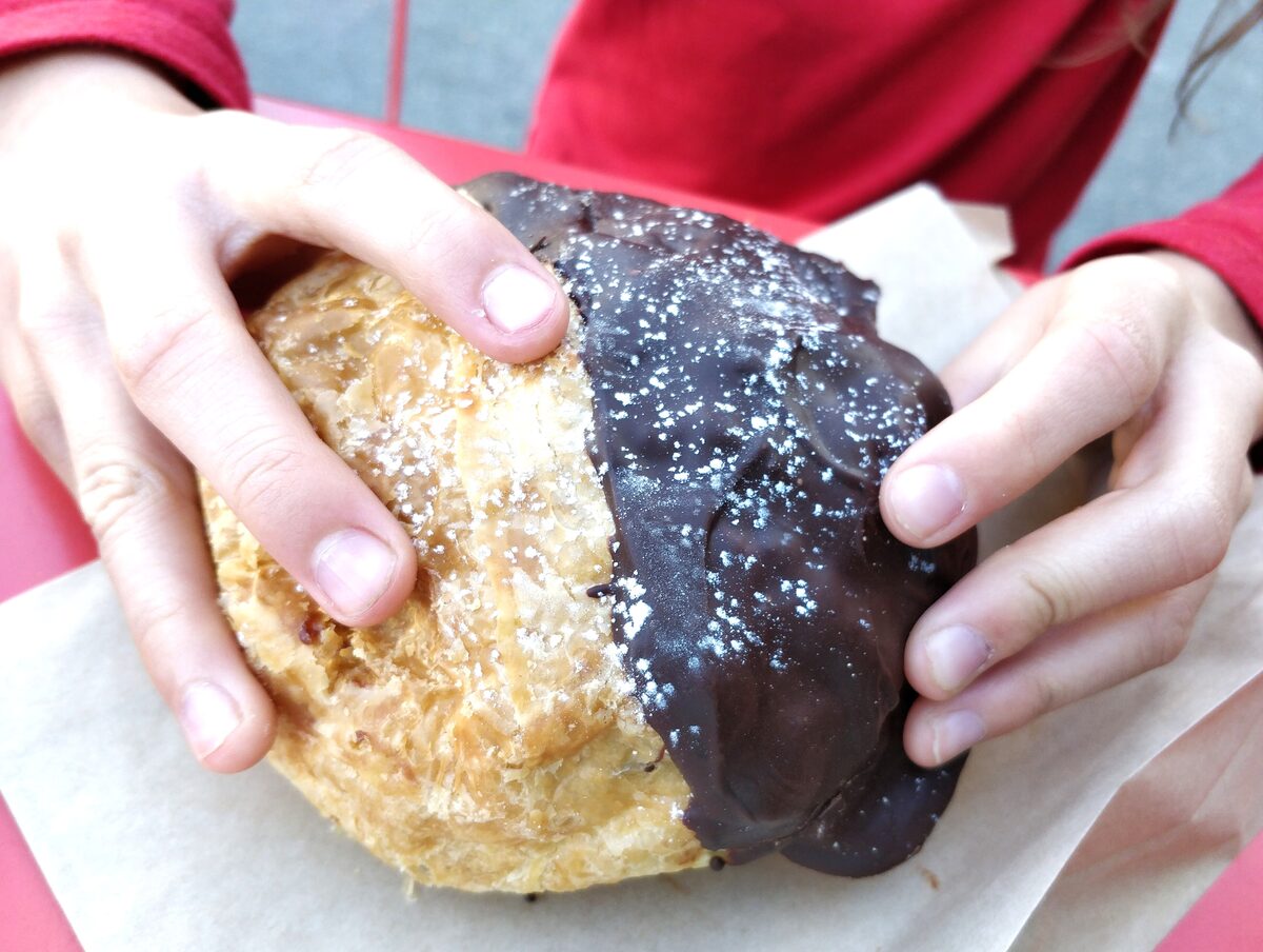 A hand-held bun half dipped in chocolate on baking paper, from Purebread