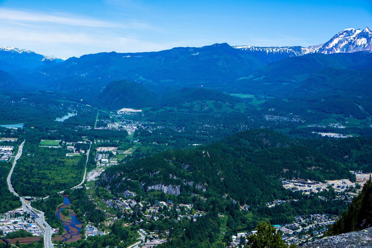 Aerial view of Squamish town in the valley below the mountains, with a snowy peak in the distance
