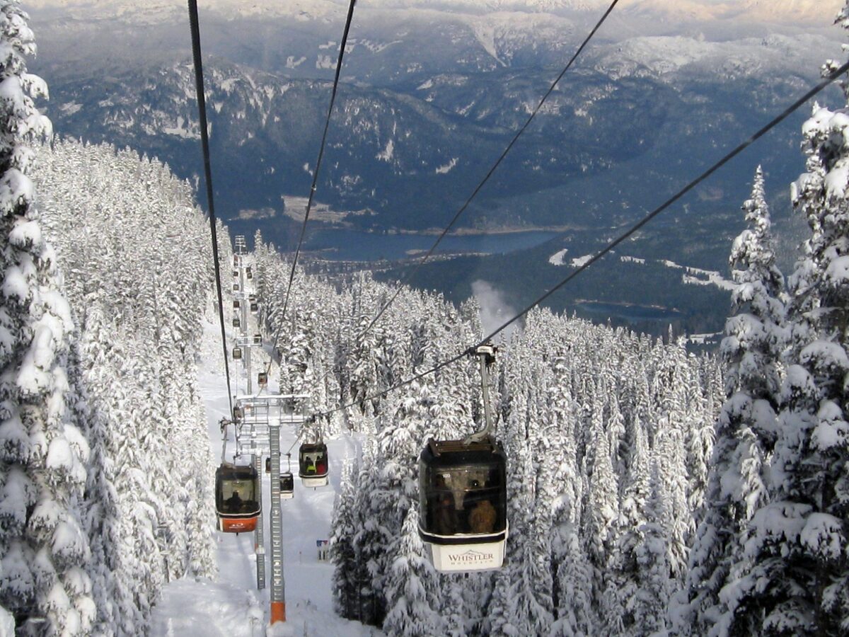 Village Gondola cabins climbing above snow-covered fir trees with the valley and mountains behind
