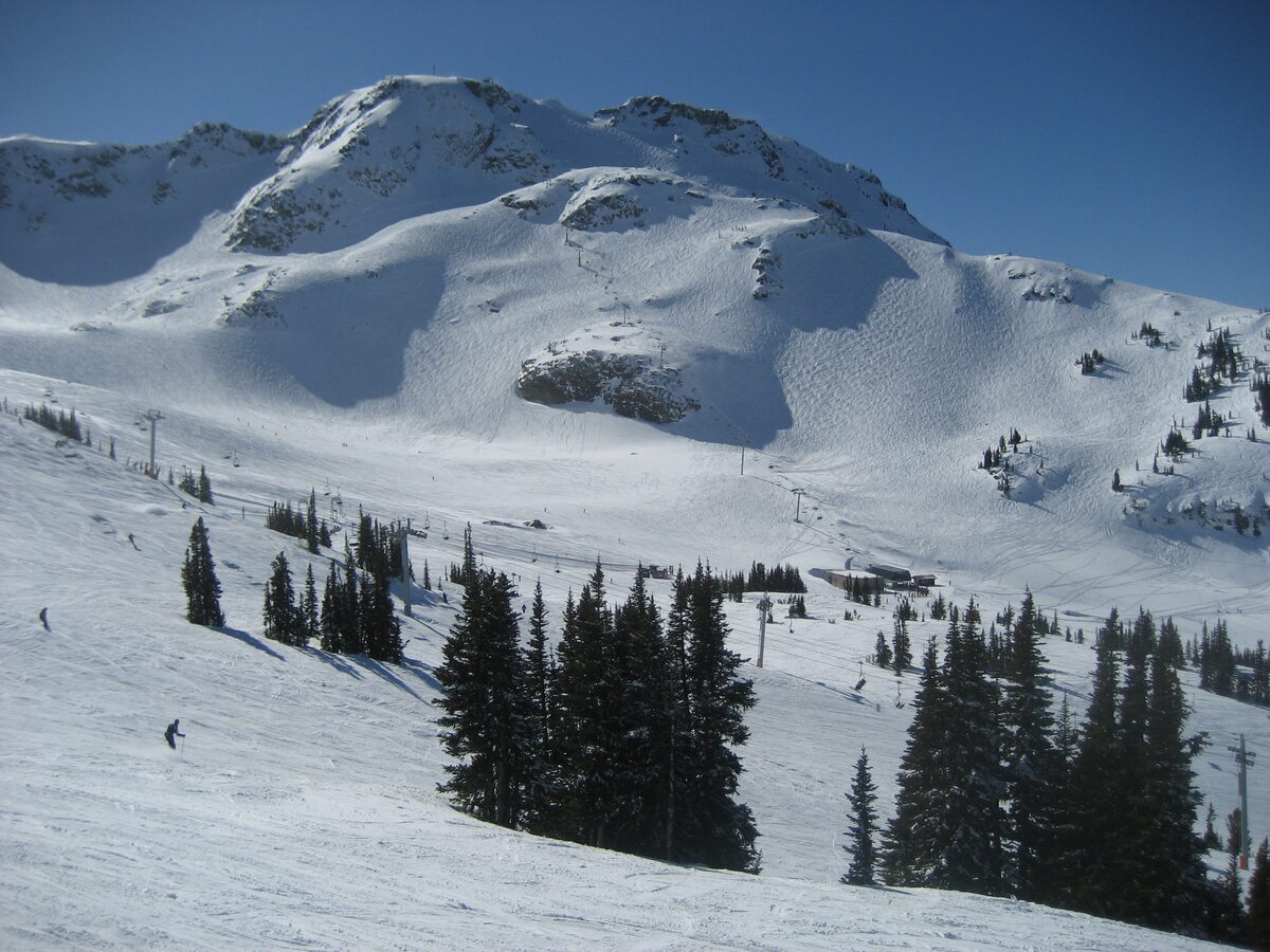 Whistler Peak under fresh snow with skiers on the slopes and a chairlift below