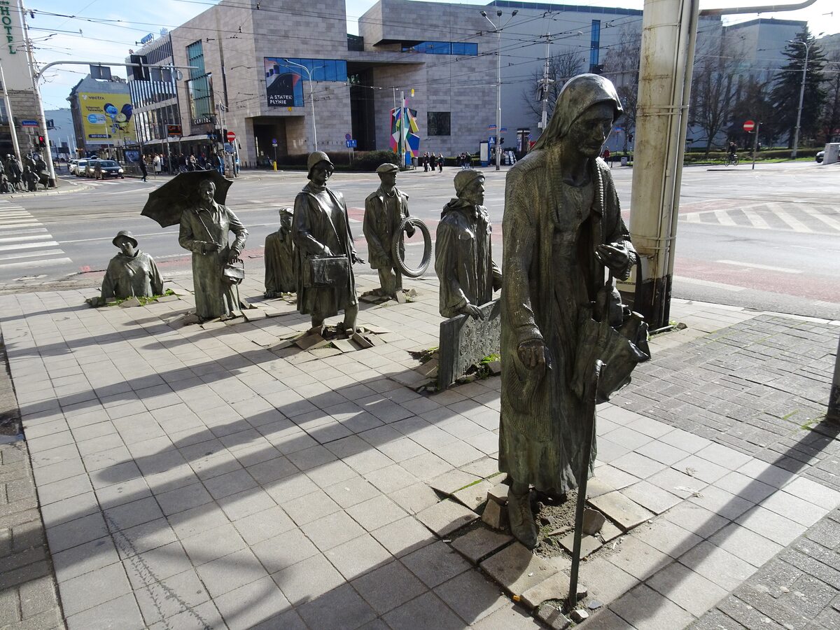The bronze figures of the Monument to the Anonymous Pedestrians walking down into the pavement on a Wrocław street corner