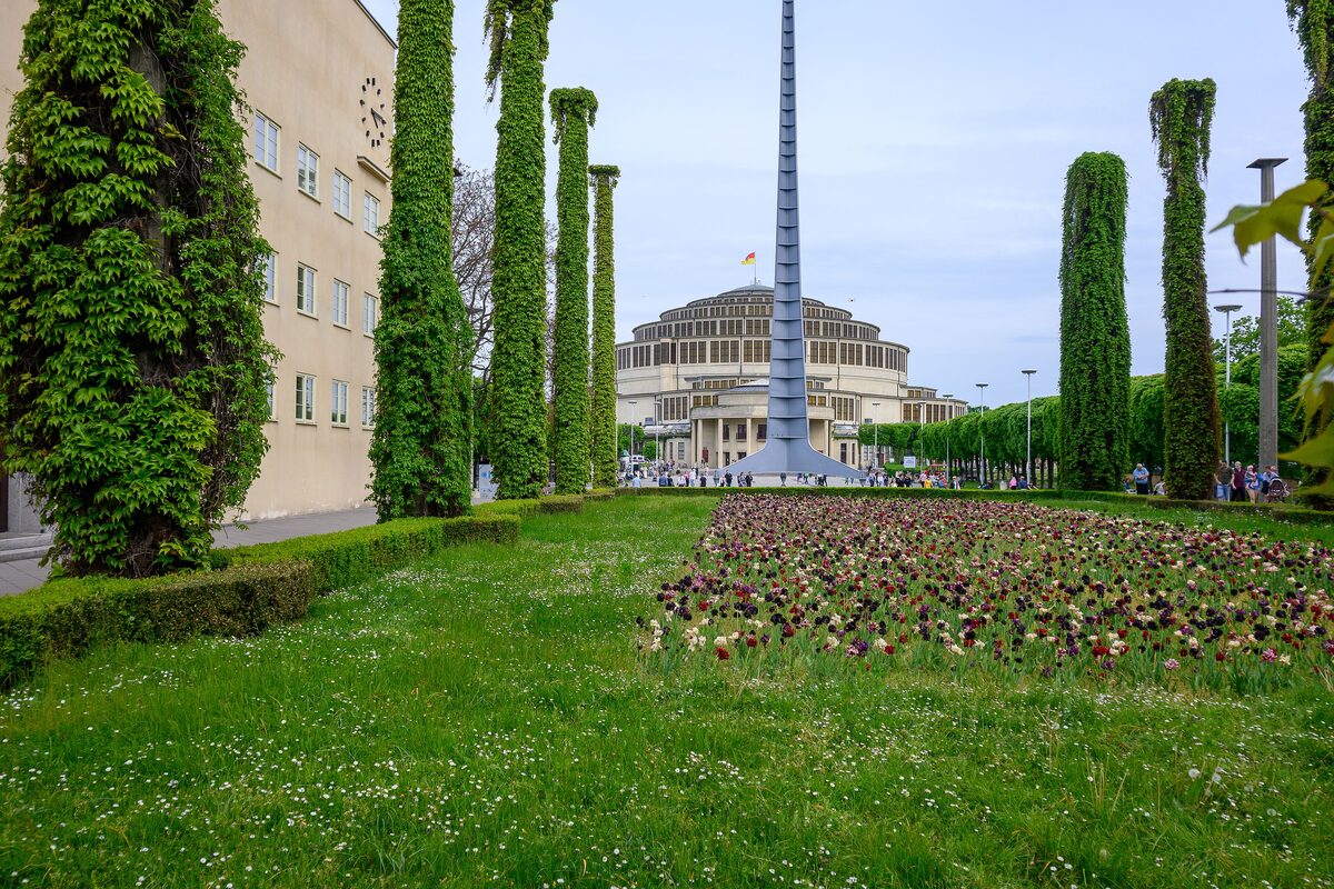 Centennial Hall and the steel Iglica spire at the end of a lawn lined with green-covered columns