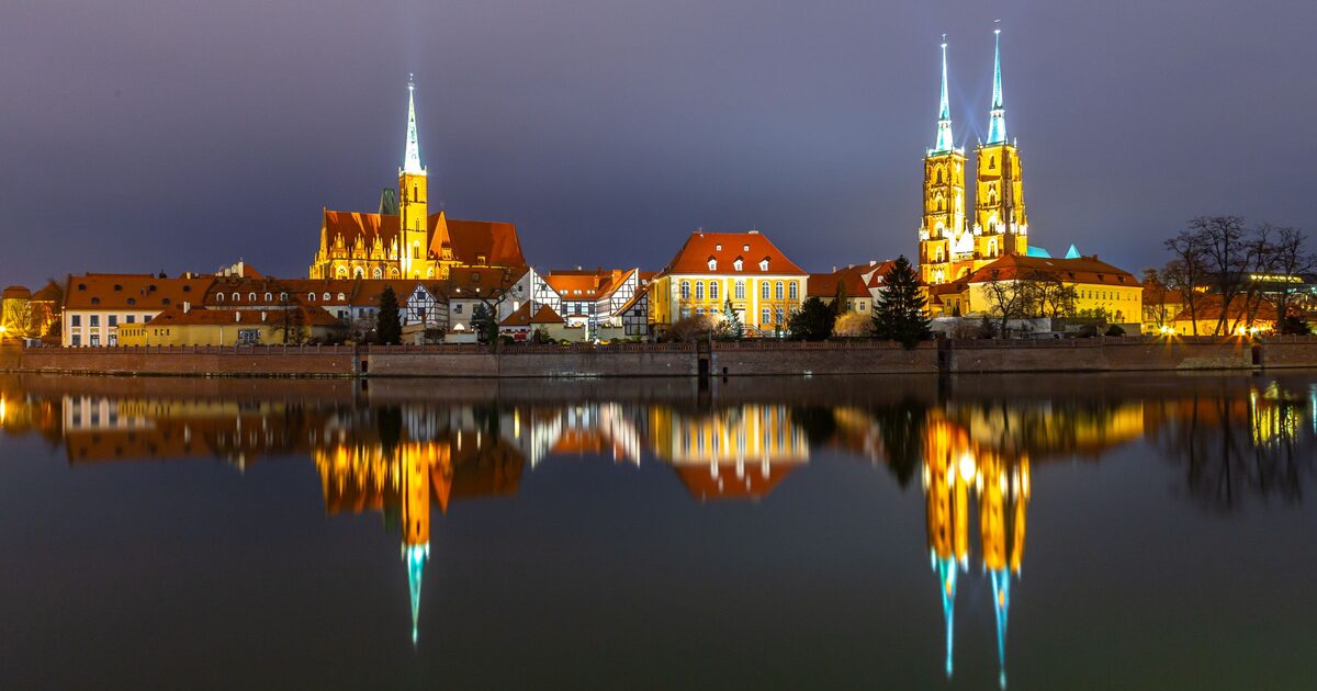 The twin spires of Wrocław Cathedral and the Church of the Holy Cross lit up at night on Cathedral Island, reflected in the Oder
