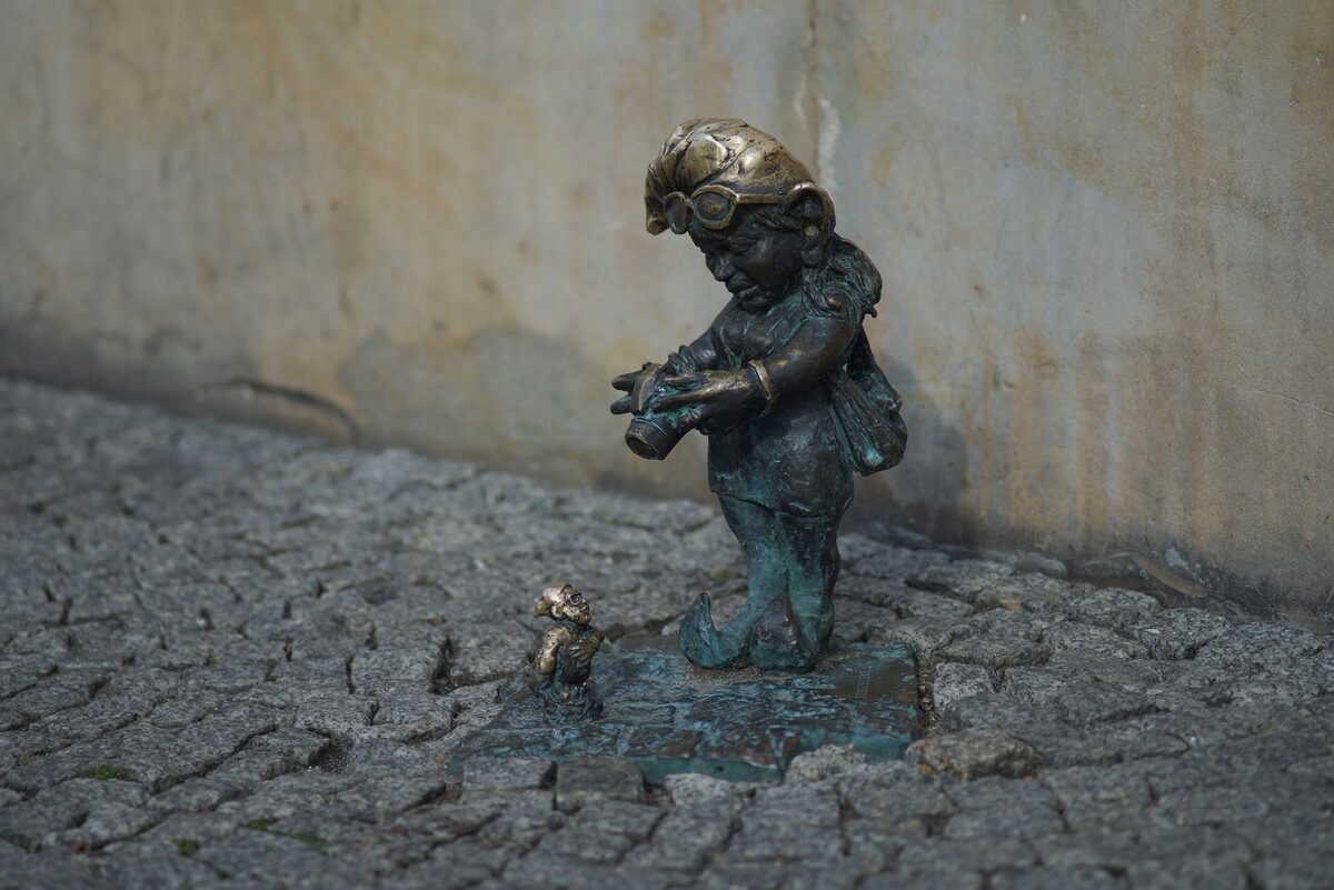 A small bronze dwarf figure with a cap and bag standing on cobblestones in Wrocław