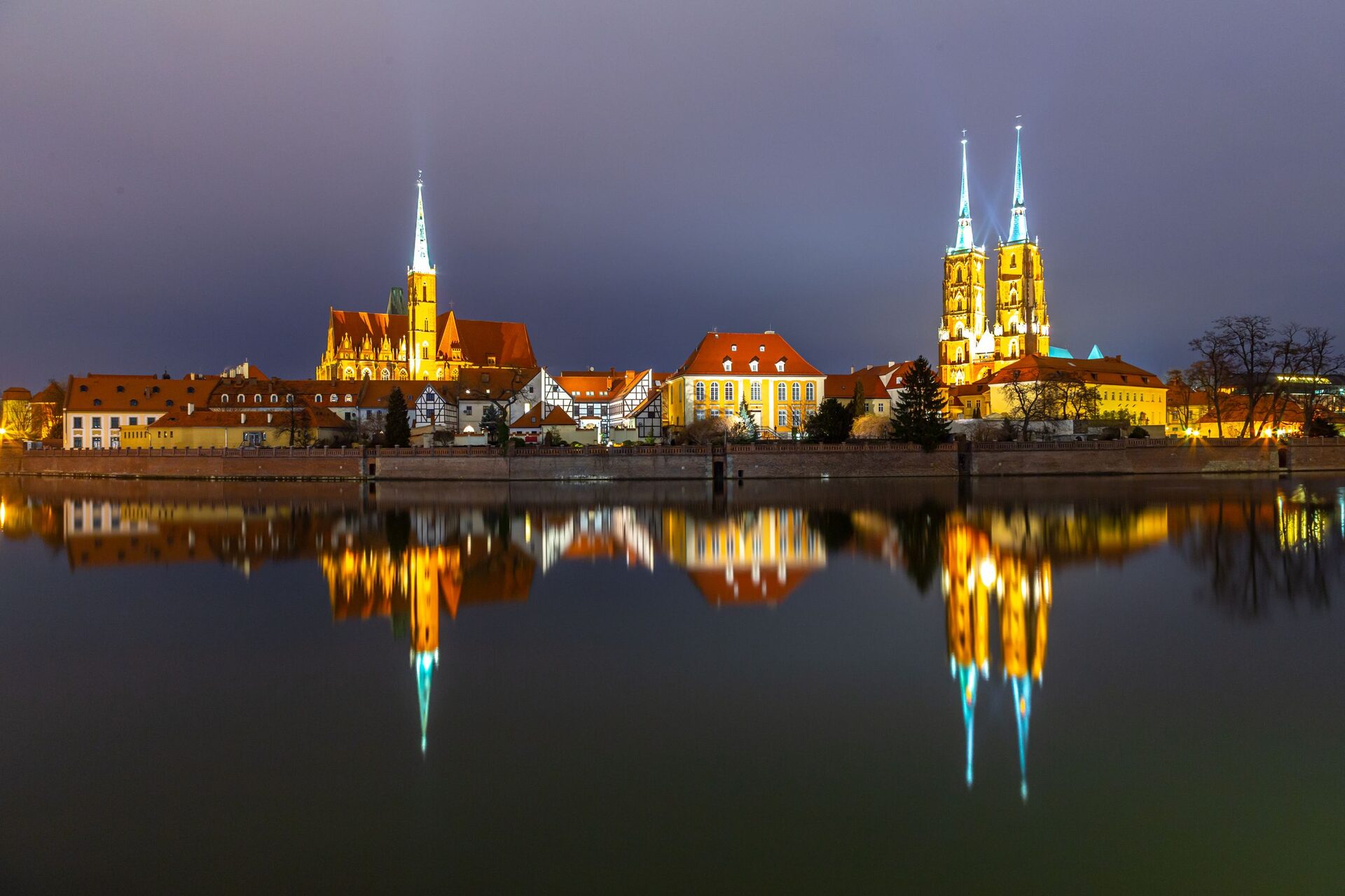 The twin spires of Wrocław Cathedral and the Church of the Holy Cross lit up at night on Cathedral Island, reflected in the Oder