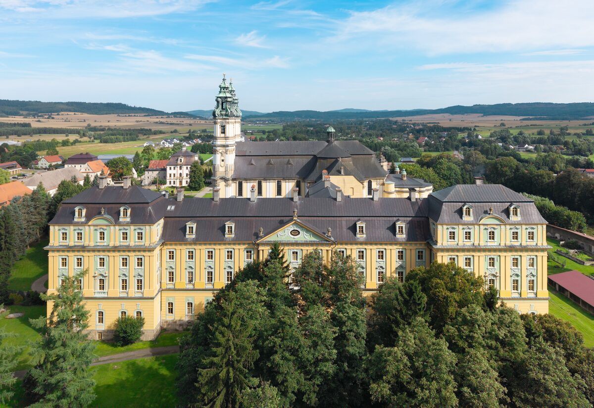 Krzeszów Abbey seen from above, a long yellow baroque monastery with the church towers behind it