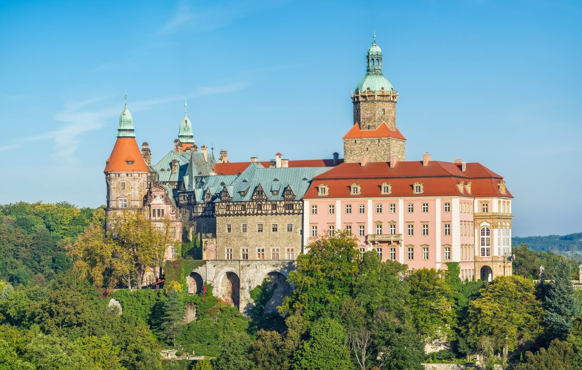 Książ Castle with its towers and pink and white wings rising above a wooded gorge